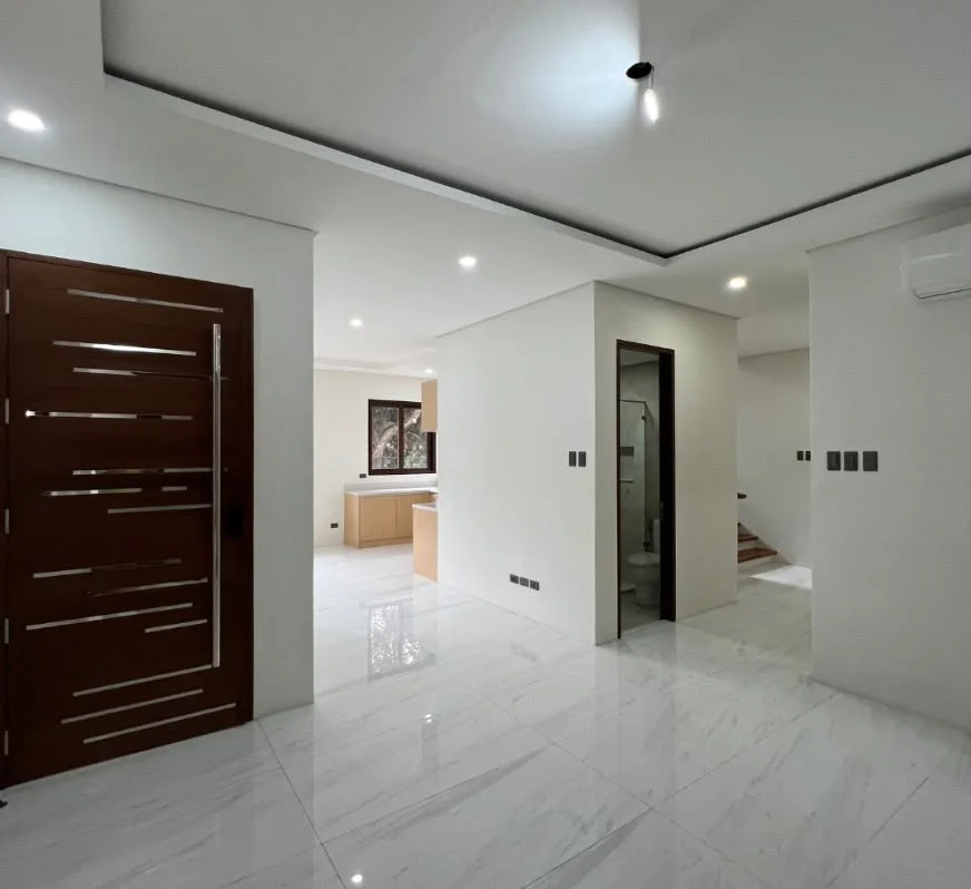 Entry hall with a dark wood front door featuring diagonal metal inlay accents, glossy white marble-look floor tile, and a view through to the kitchen and staircase beyond