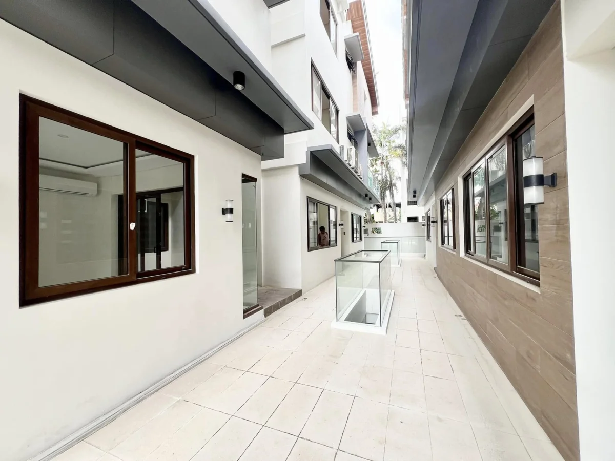 Ground-level covered walkway between units, tiled floor set with rectangular glass skylight panels, a person visible through a window partway down the corridor