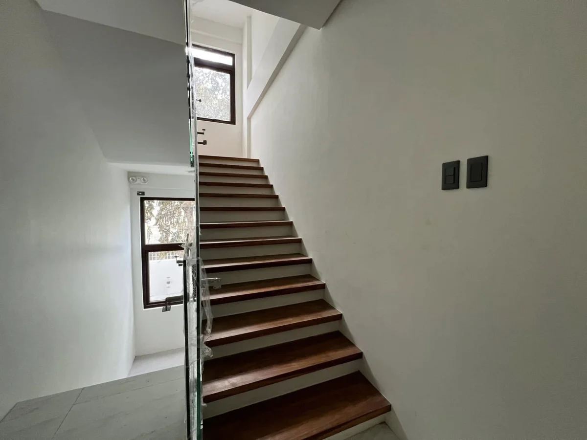 Interior staircase with dark wood treads and white risers, a glass balustrade still wrapped in protective film, and a tall window looking out to trees