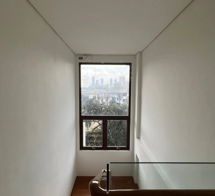 Stairwell landing with a tall window framing a view of the Quezon City skyline and surrounding rooftops, glass balustrade with a wood handrail visible below